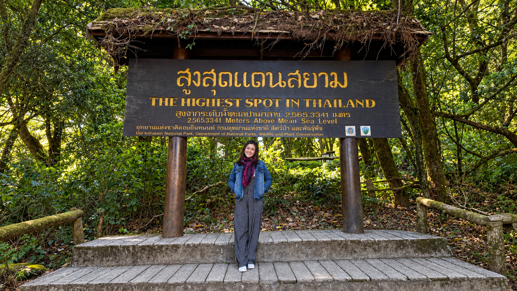 A traveler standing beneath the summit sign at Doi Inthanon National Park, Thailand.